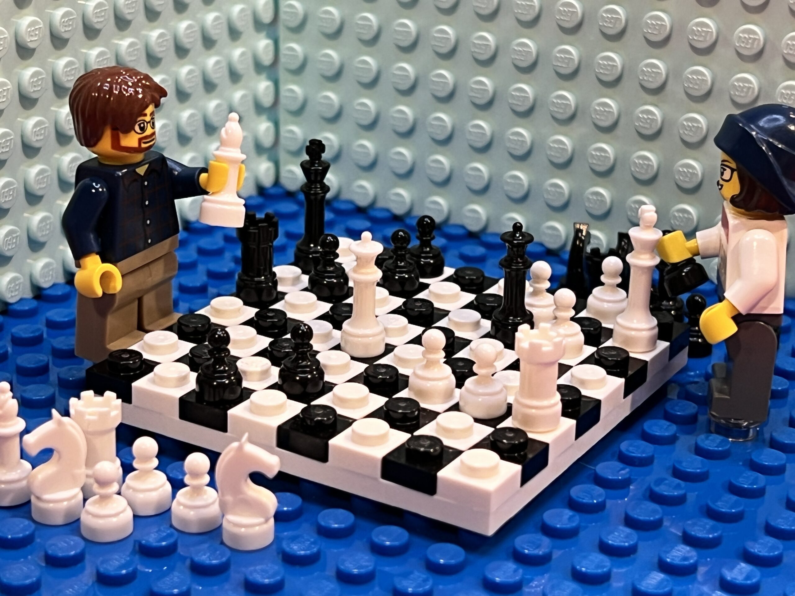 Two Lego people playing chess with a black and white Lego chessboard and pieces