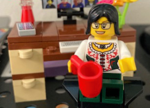 Lego Kate at her Lego desk, with computer, lamp, vase of flowers, and a coffee mug